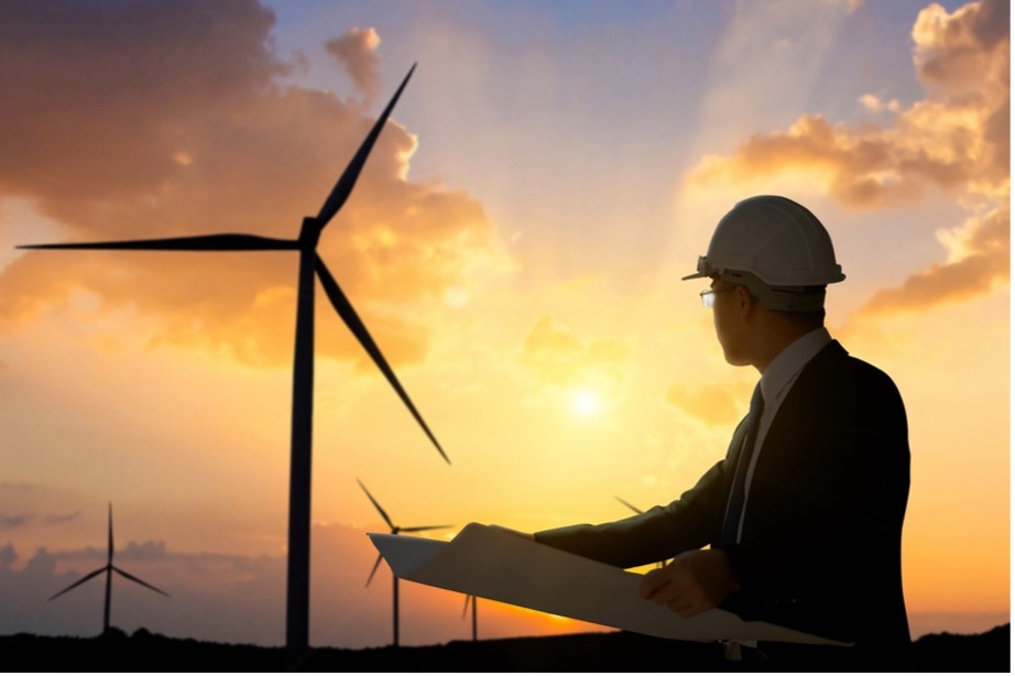 A person in a suit and hard hat looking at windmills